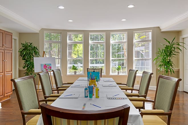 A well-lit conference room with a meeting table surrounded by chairs, set up with notepads and pens.