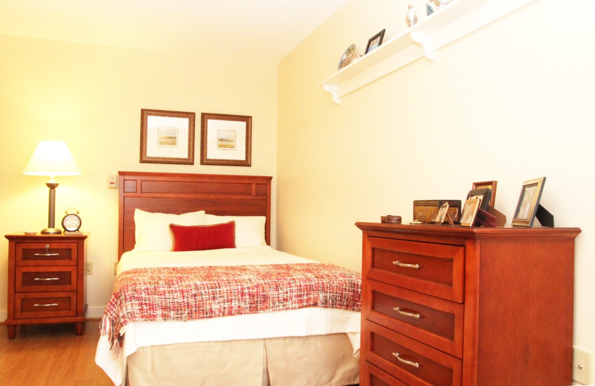 A cozy bedroom with a wooden bed and dresser, complemented by framed artwork and shelf decor.