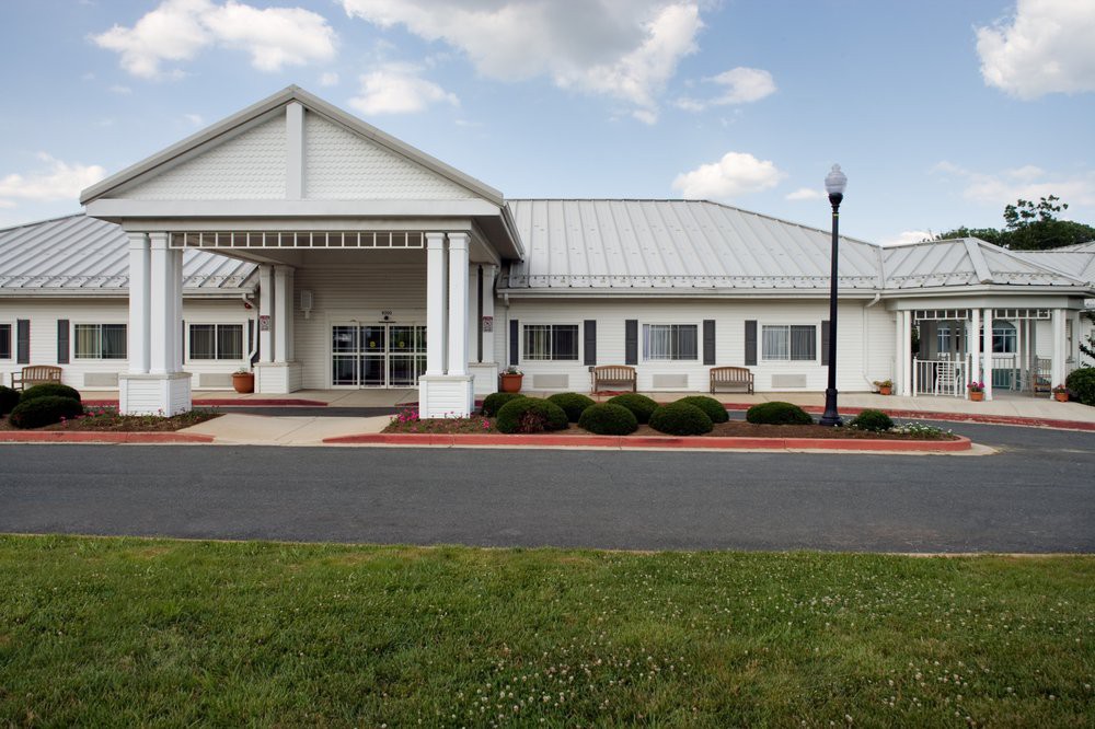 A white building with a modern design featuring a prominent entrance, surrounded by well-kept landscaping and under a partly cloudy sky.