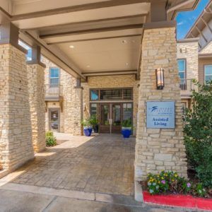 Entrance of a stone building with a covered walkway and landscaped surroundings.