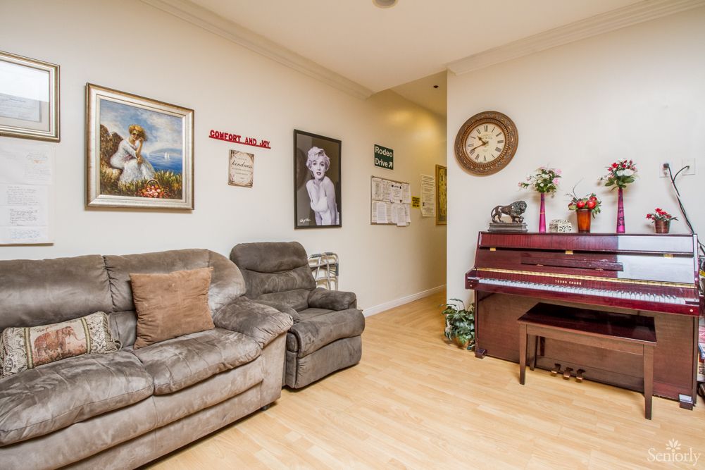 A cozy living room featuring a sofa and a piano, adorned with wall art and a decorative clock.
