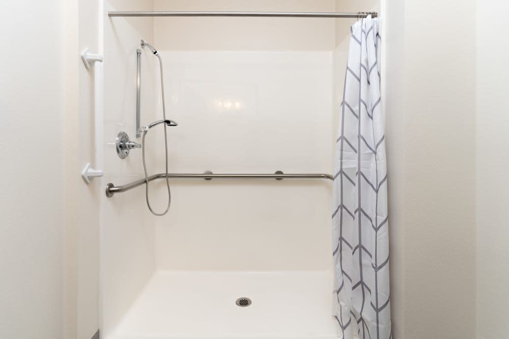 An accessible bathroom with a shower, featuring grab bars and a handheld shower head.