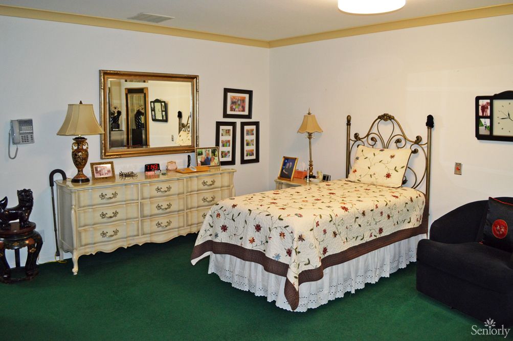 A cozy bedroom with a bed, dresser, and mirror. The room features warm lighting and decorative touches.
