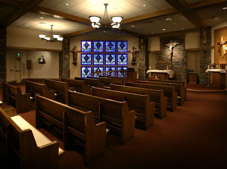 Interior of a chapel featuring wooden pews, stained glass windows, and an altar with a crucifix.