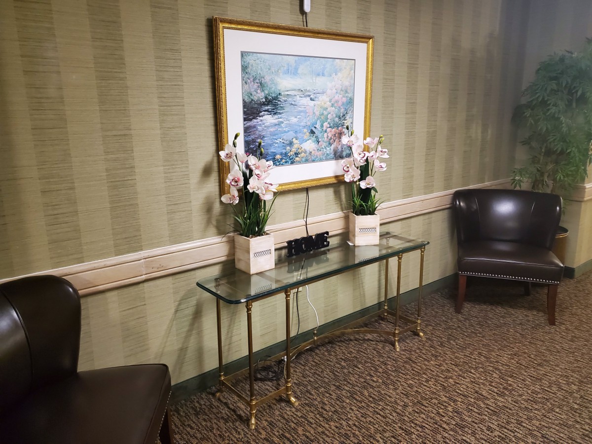 A well-decorated interior space featuring a glass table with potted flowers and a landscape painting above it.
