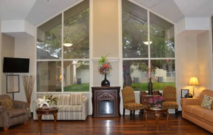 A cozy living room with large windows, featuring a sofa, chairs, a fireplace, and decorative elements.
