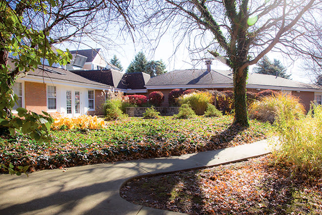 A residential home with a landscaped yard, featuring trees and an autumn pathway.