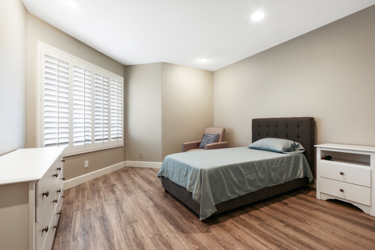 A minimalist bedroom with a neatly made bed and hardwood flooring.