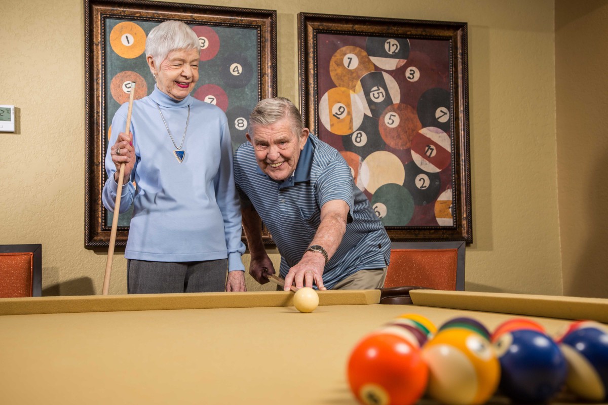 An elderly couple enjoying a game of pool together.