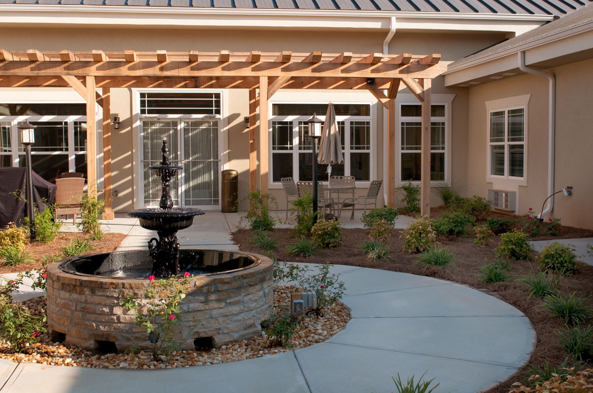 A serene courtyard featuring a central fountain, surrounded by a pergola and well-maintained garden landscaping.