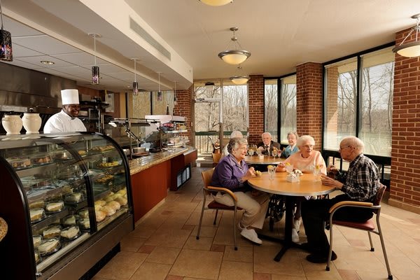 A group of seniors enjoying a conversation in a cozy cafe with a dessert display in the background.