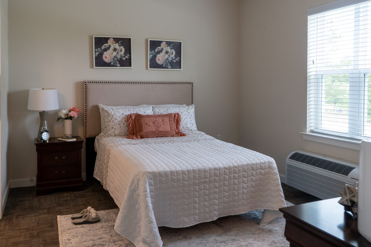 A cozy, minimalist bedroom with a neatly made bed featuring white bedding and decorative pillows, accompanied by wall art and nightstands.