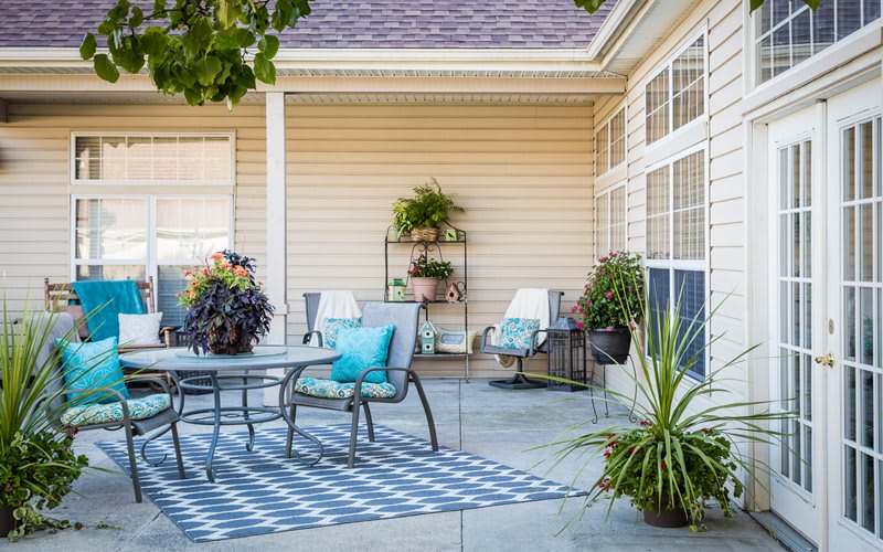 A cozy outdoor patio with a dining table, chairs, and lush plants.