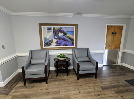 A cozy waiting area featuring two grey chairs, a small table, and decorative artwork on the wall.