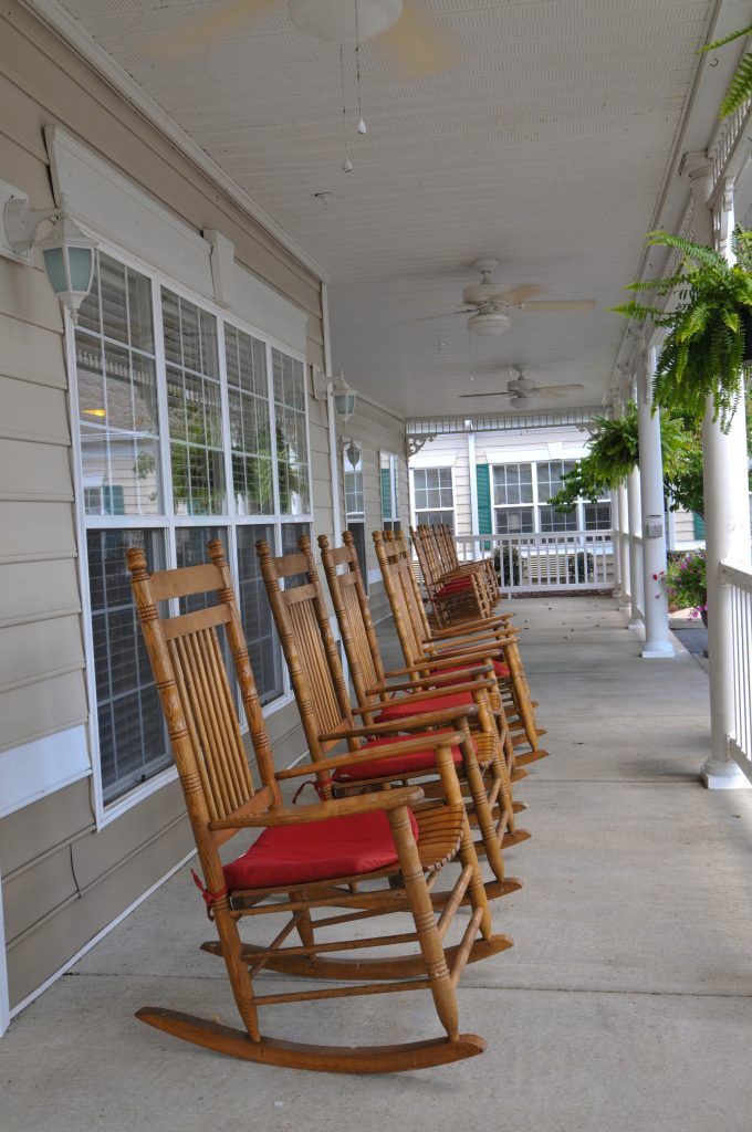 A row of wooden rocking chairs with red cushions on a cozy porch.