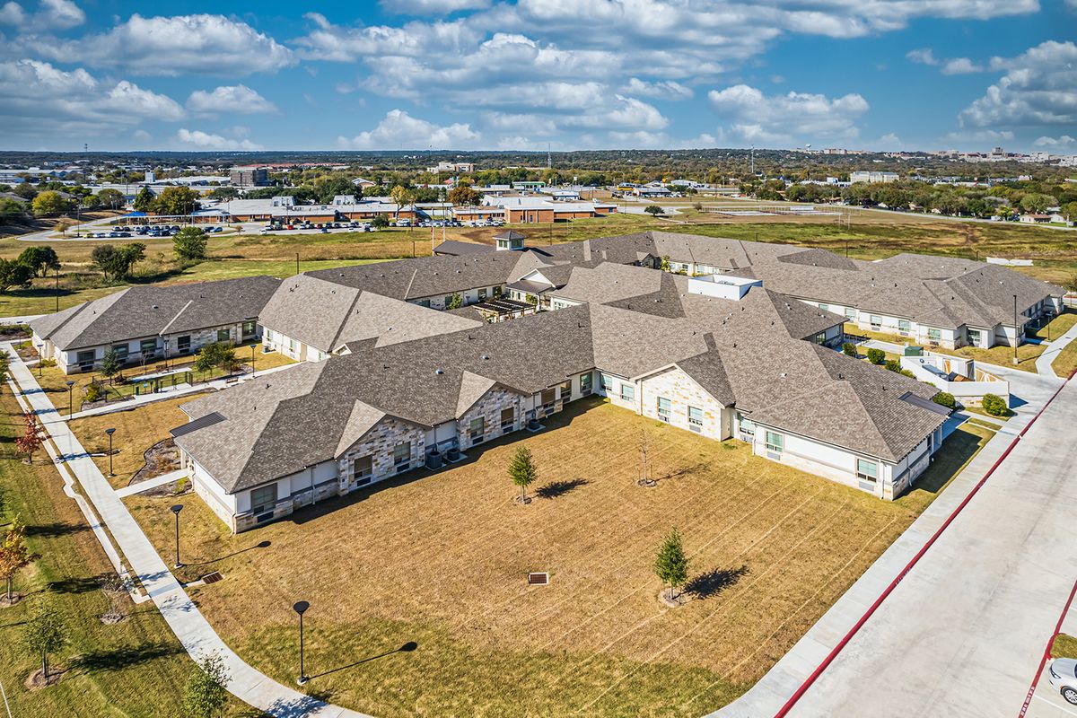 Aerial view of a residential building complex with a spacious yard in a suburban area under a cloudy sky.