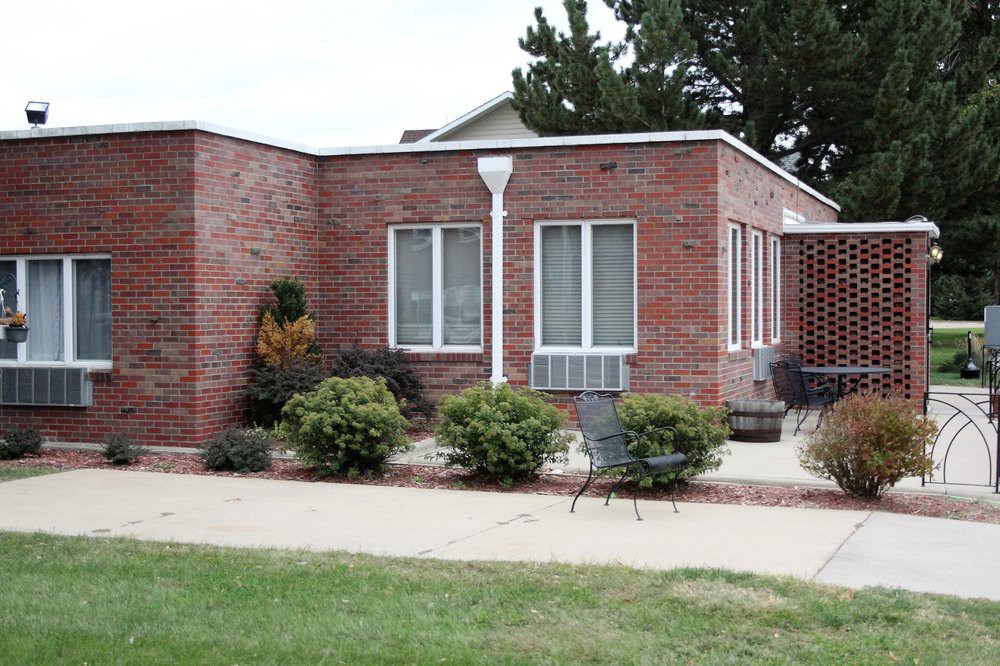 A brick house with large windows and a small patio area surrounded by greenery.
