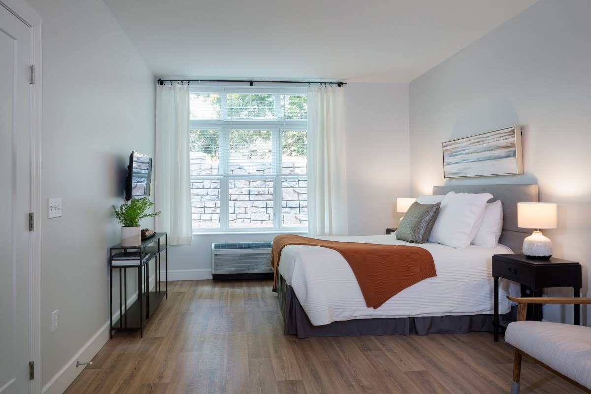 A modern and minimalist bedroom with a large window, hardwood floors, and tasteful decor.