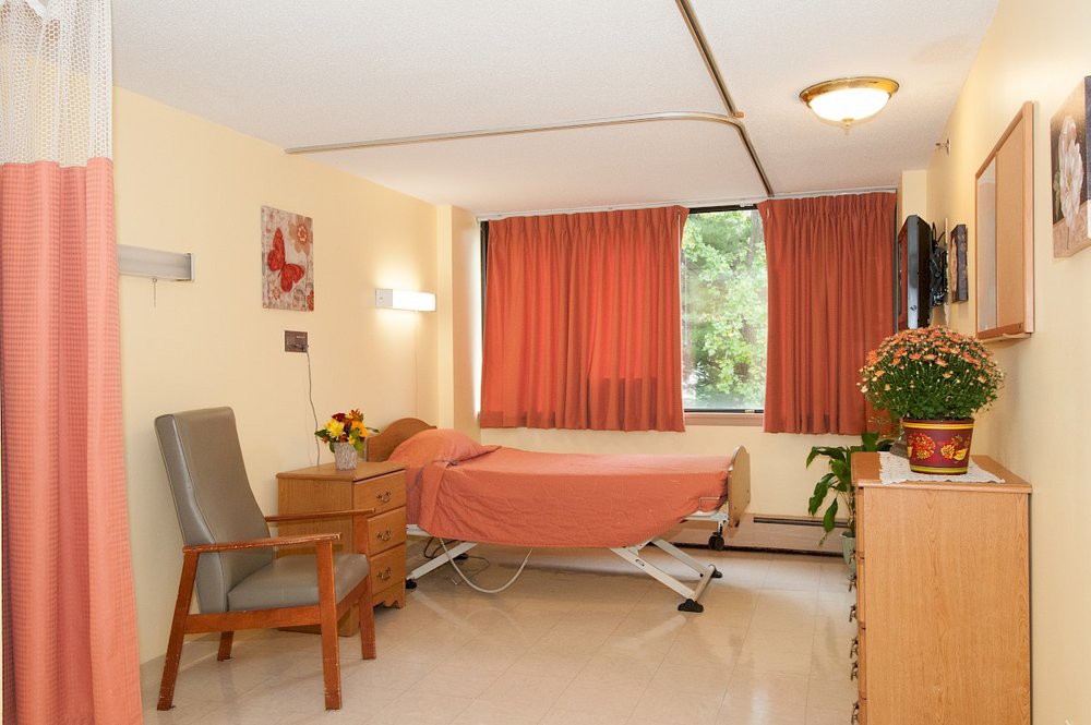 A tidy hospital room with a single bed, chair, and window with curtains.