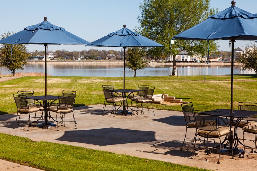 A peaceful outdoor patio with tables and blue umbrellas overlooking a lake.