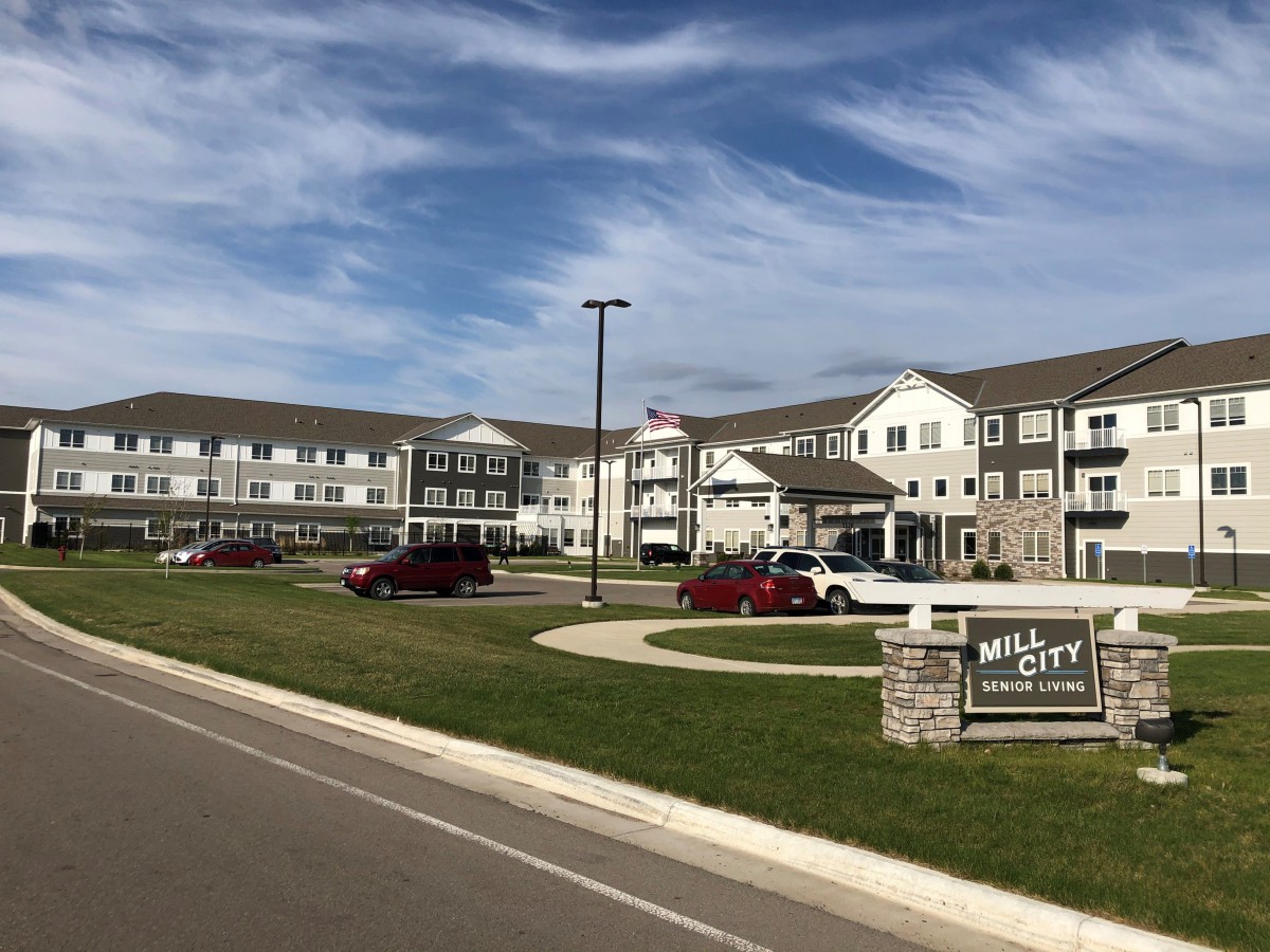 A large residential building with a parking lot and well-maintained lawn under a partly cloudy sky.
