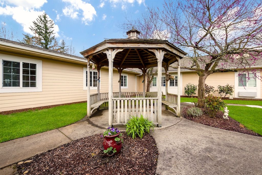 A charming gazebo in a well-maintained garden, surrounded by trees and adjacent to a house.