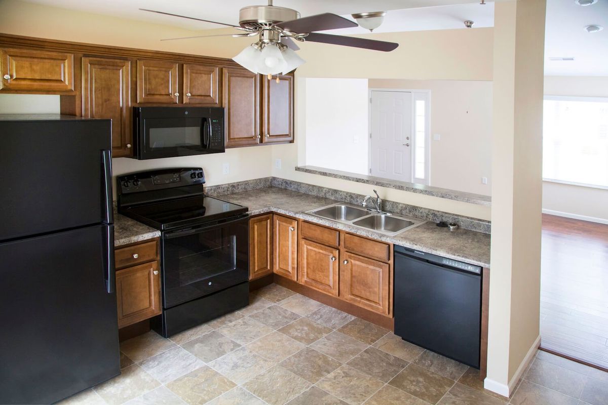 A modern kitchen with wood cabinets, black appliances, and a ceiling fan.