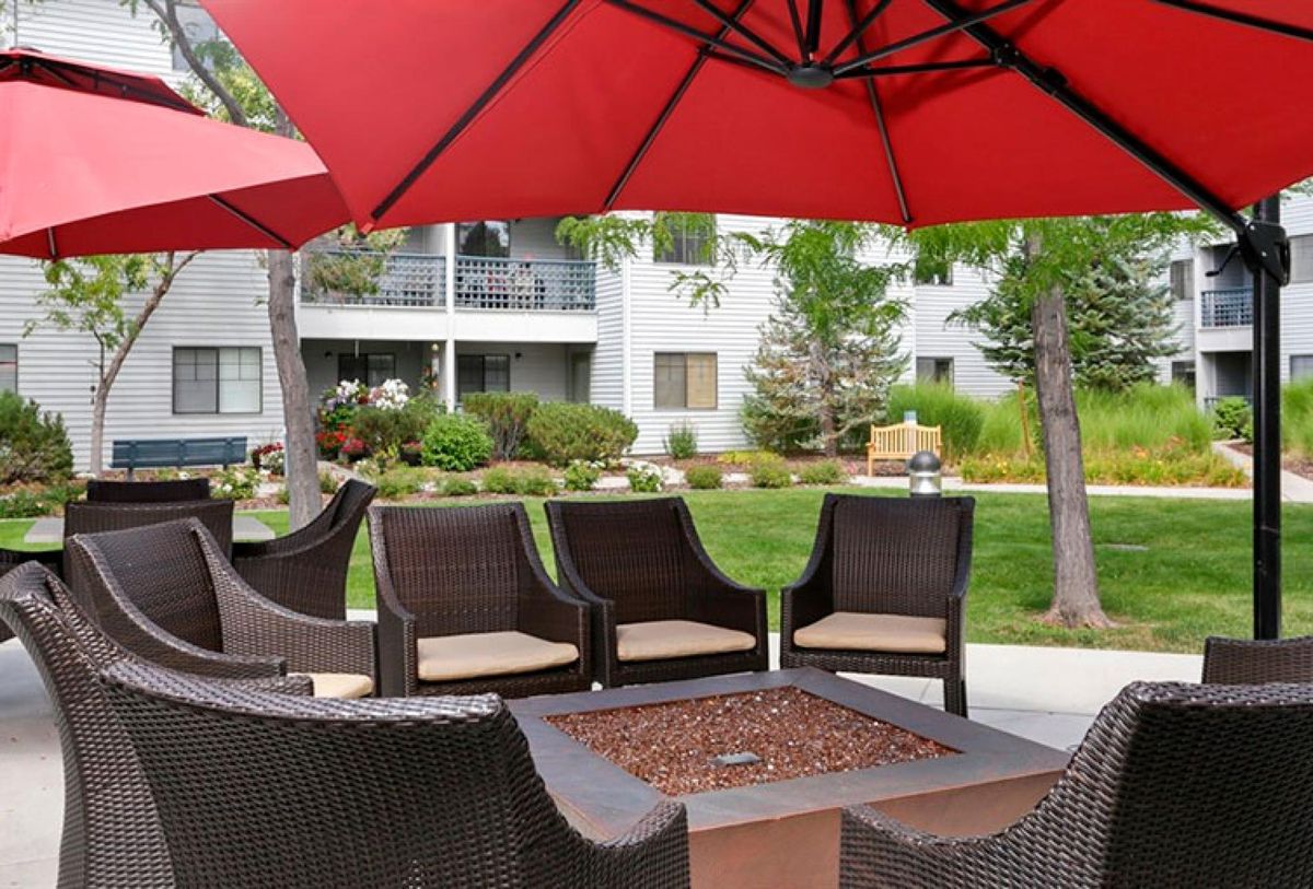 Outdoor patio area with chairs and a fire pit under a red umbrella.