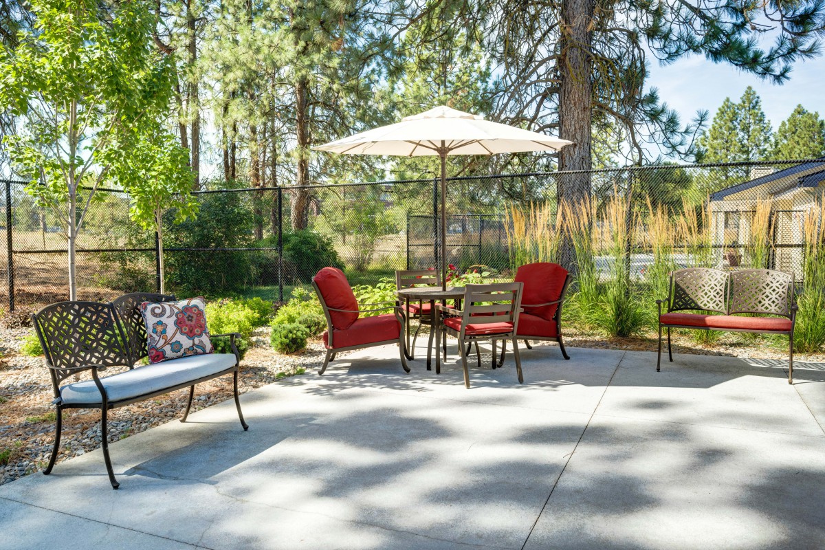 A cozy patio setup with red cushioned chairs surrounding a table under a large umbrella, nestled in a lush garden setting.