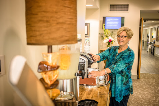 A cheerful woman prepares coffee at a cozy beverage station, illuminated by a stylish lamp.