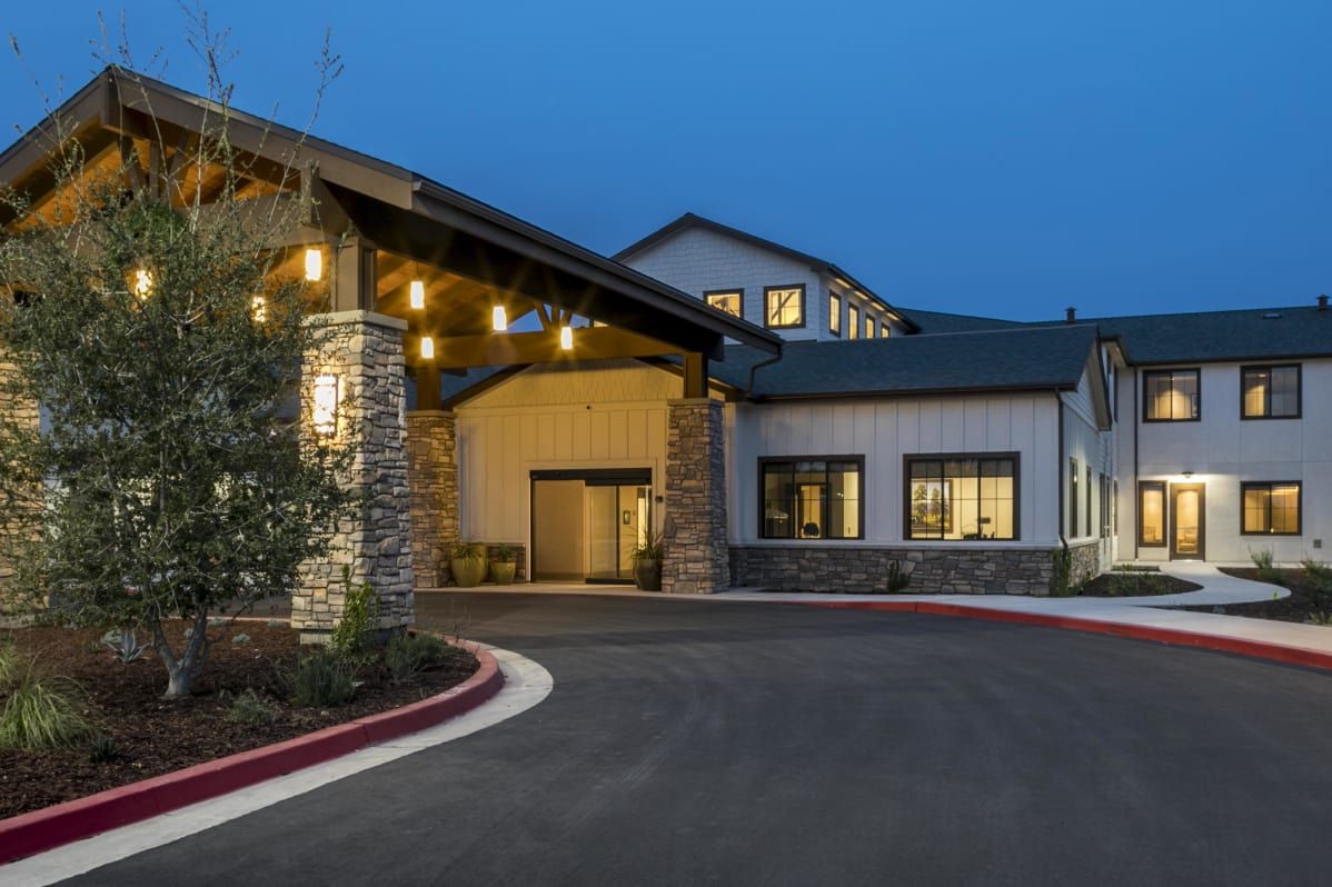 A well-lit building entrance with a curved driveway during the evening.
