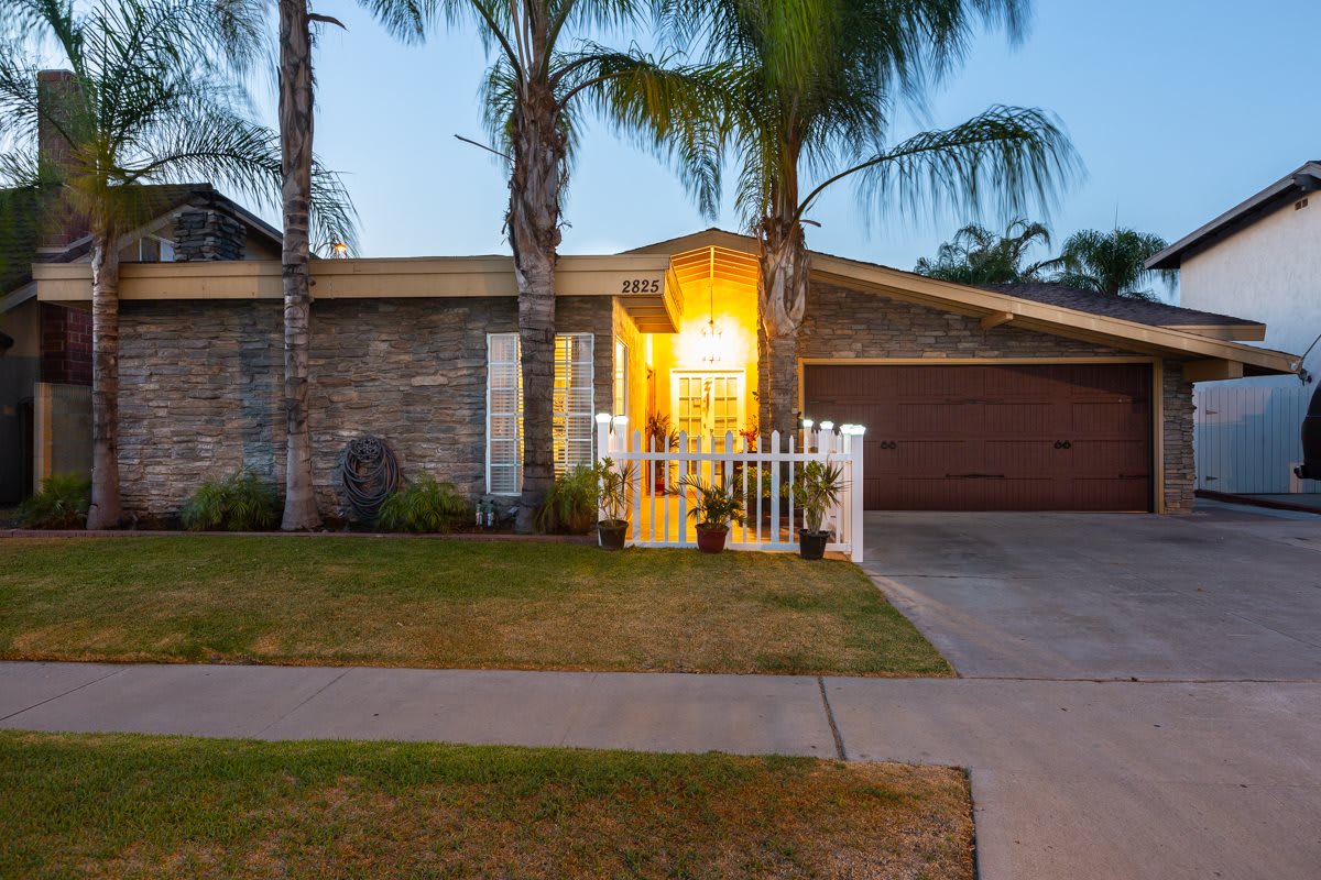 A suburban house in the evening with palm trees and a well-lit entrance.