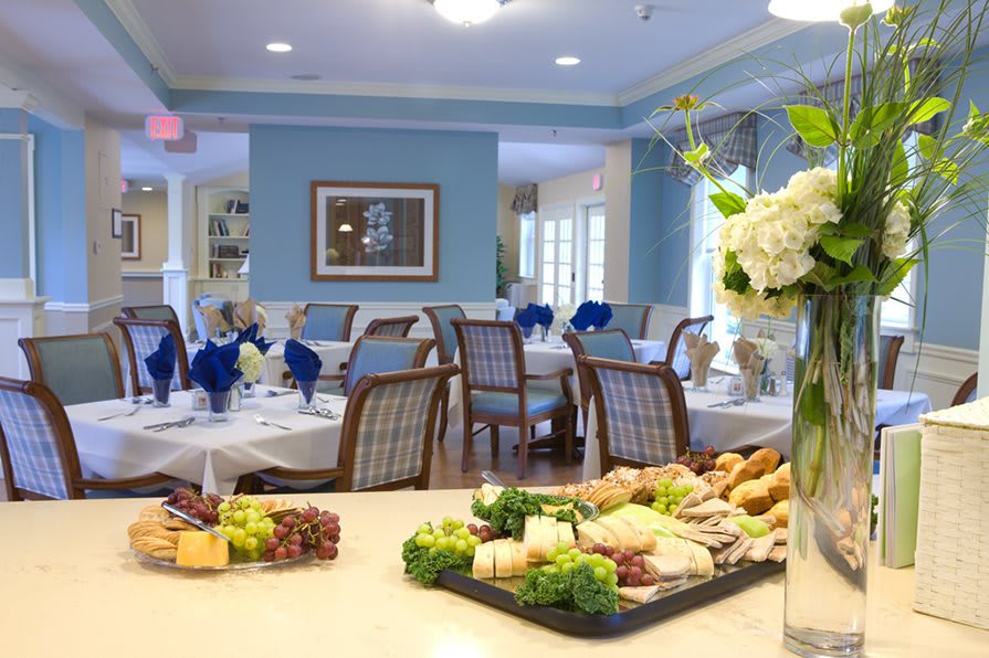 A beautifully set dining room with elegant tables and a tray of assorted sandwiches and fruits.