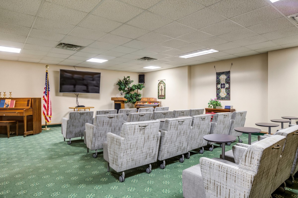 A well-lit waiting room with rows of chairs, a television on the wall, and decorative plants.