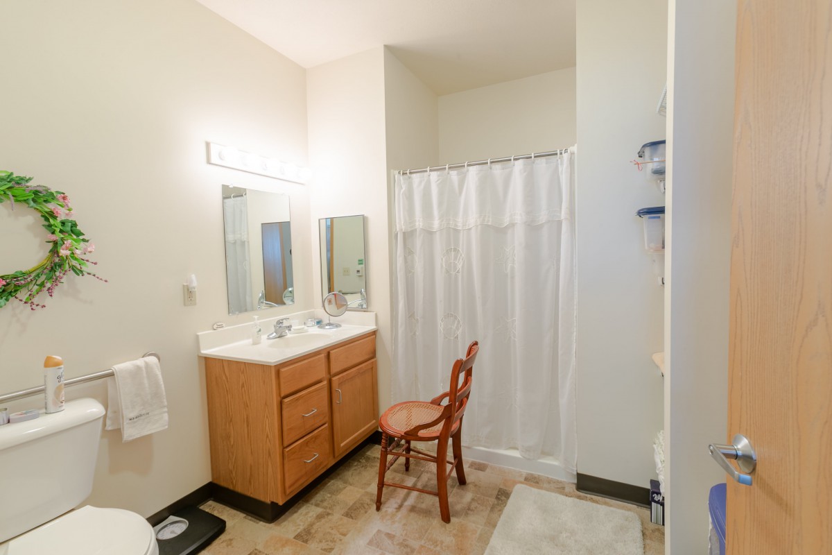 A bathroom with a sink, mirror, shower, and a wooden chair.