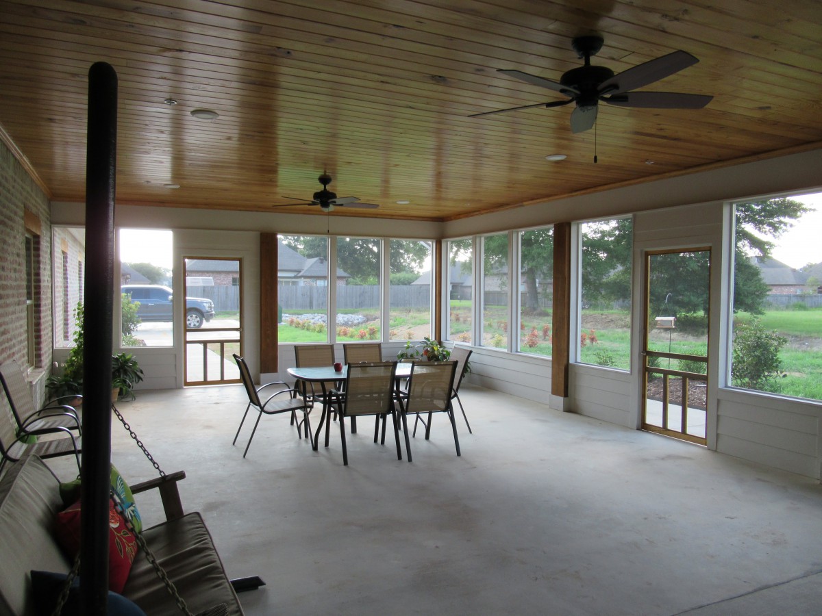 A spacious sunroom with a dining table and chairs, featuring large windows and ceiling fans.