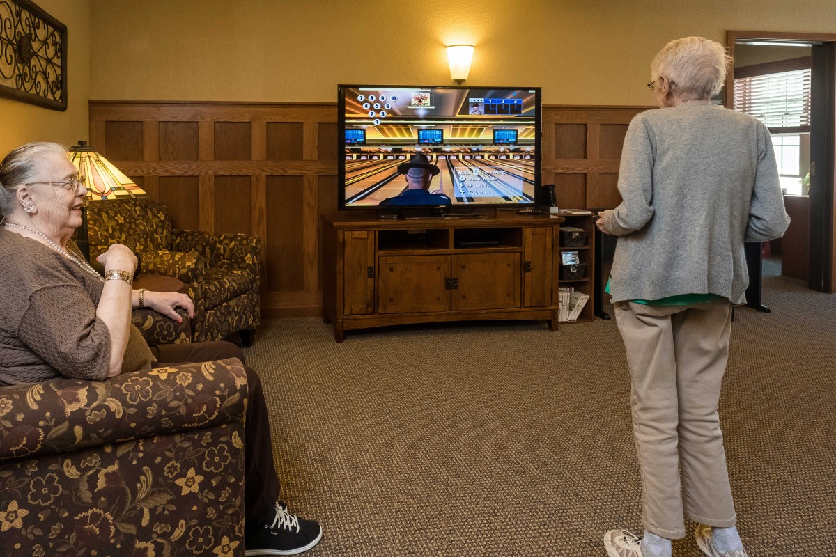 Two seniors enjoying a virtual bowling game on a gaming console in the living room.