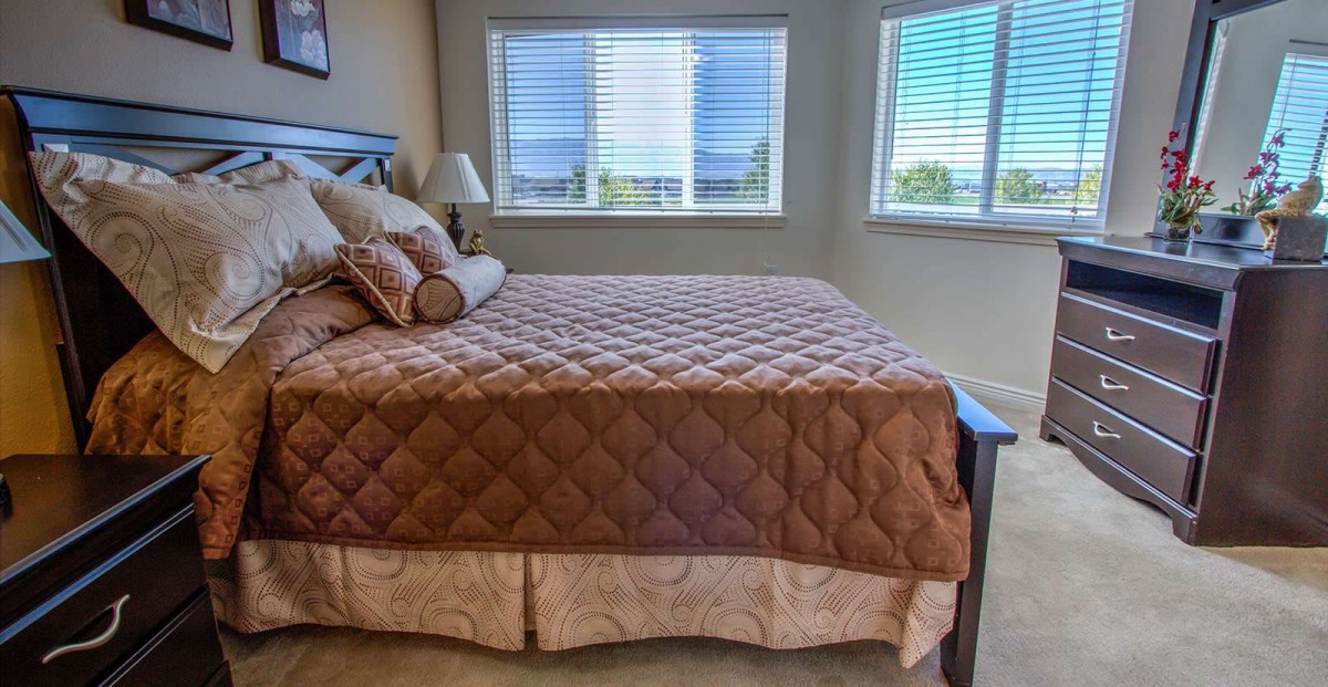 A cozy bedroom with a large bed and multiple windows, featuring a quilted bedspread and decorative pillows.