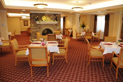 A cozy dining room interior with tables and chairs arranged around a fireplace.