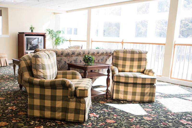 A cozy living room with plaid-patterned chairs, a floral sofa, and a wooden table bathed in sunlight.