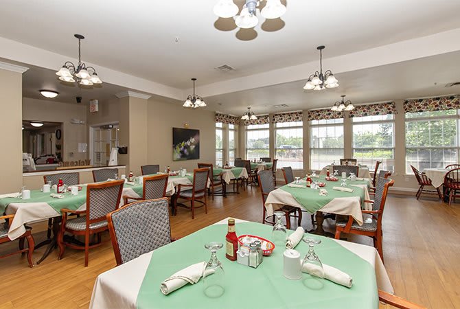 A well-lit dining area with neatly arranged tables and chairs, featuring large windows and elegant decor.