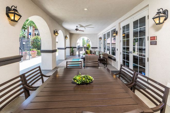 A cozy outdoor patio with a large dining table, surrounded by chairs and decorated with plants.