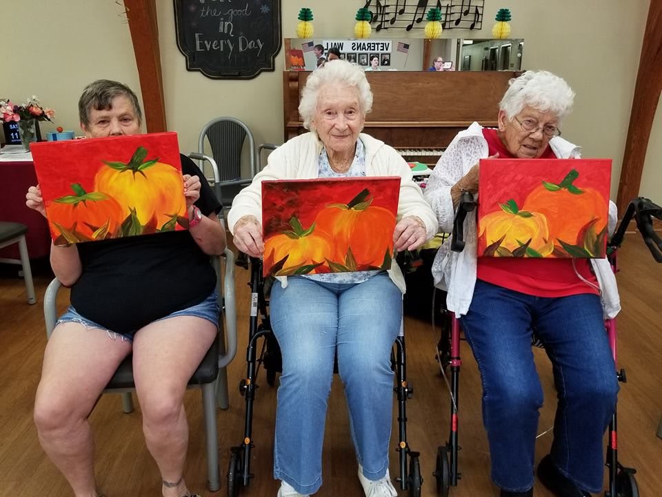 A group of seniors proudly displaying their autumn-themed paintings during a group art activity.