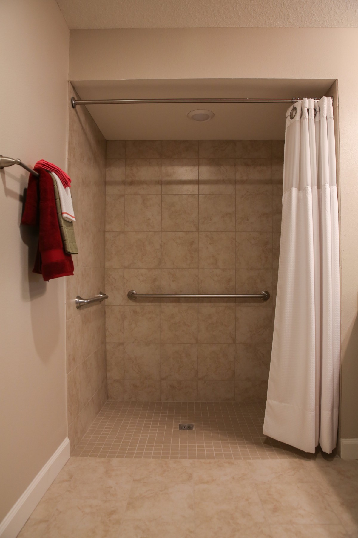A bathroom shower with a white curtain, beige tiled walls, and a grab bar for support.