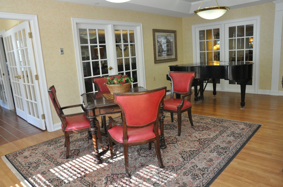 A well-designed dining room featuring red upholstered chairs, a wooden table, and a grand piano on a patterned rug.