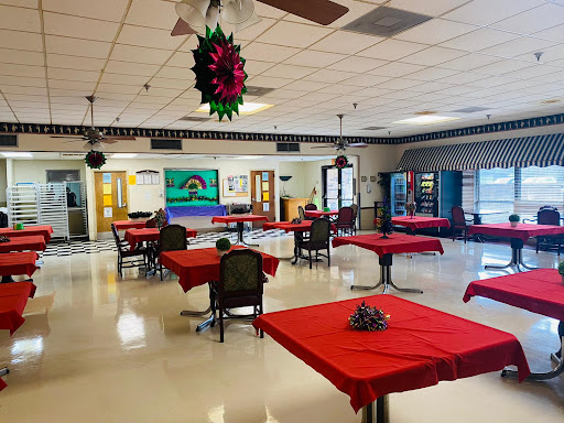 A spacious dining area set up with red tablecloths, featuring a few tables and vending machines in the background.