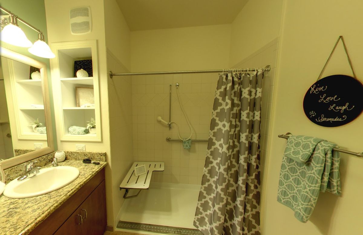 A bathroom featuring a shower with grab bars and a folding seat for accessibility.