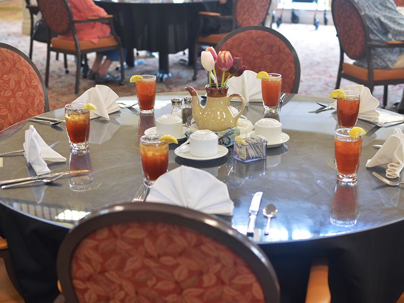 A round dining table set with glasses of iced tea and arranged tableware in a restaurant setting.