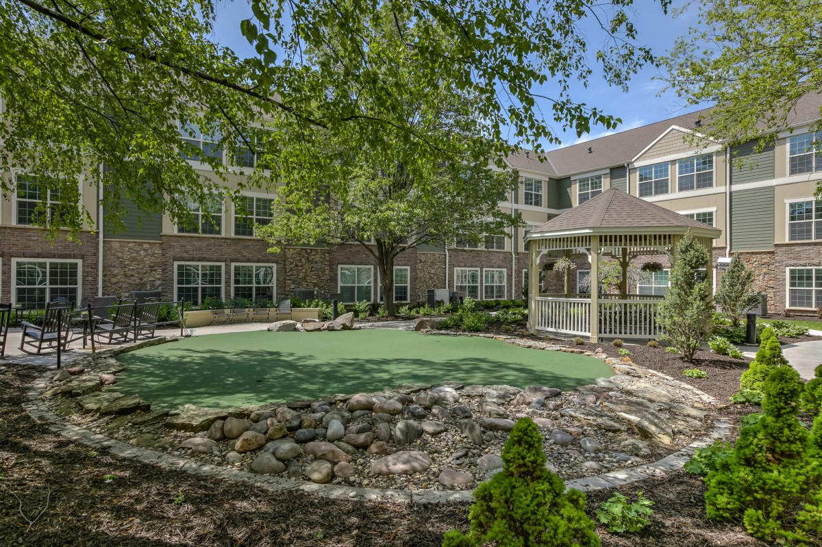 A serene garden with a gazebo and surrounding building, lush greenery and open lawn.