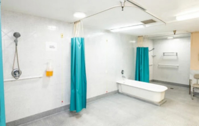A sterile hospital bathroom featuring a bathtub and teal shower curtain.